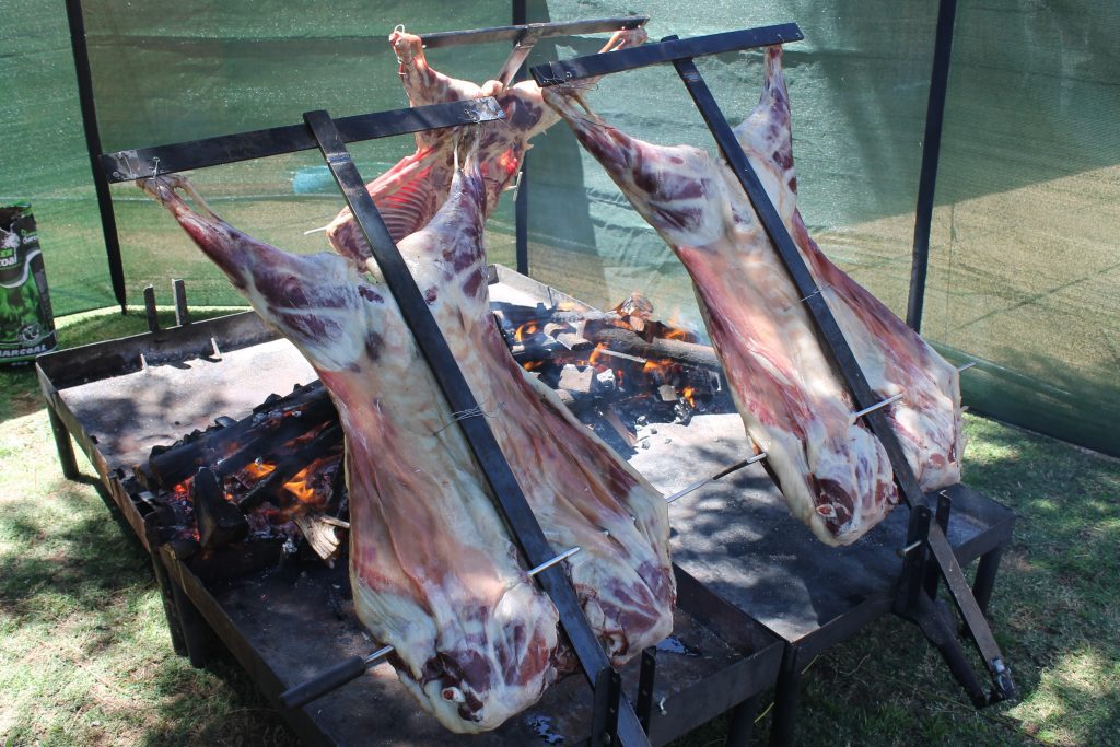 Multiple whole lambs on rotisserie spits roasting over an open fire for a large spitbraai catering event by Pedros Asado